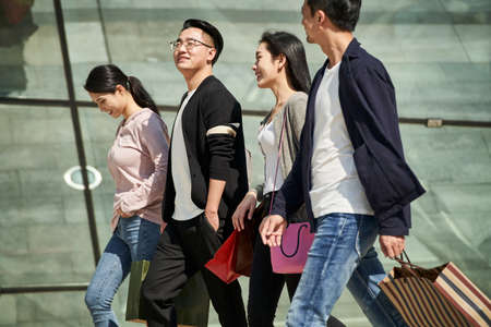 high angle view of group of four young asian people chatting talking conversing while walking on street with shopping bags in handsの写真素材