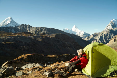 asian man male camper sitting in tent enjoying the early morning sunlight in yading national park,...