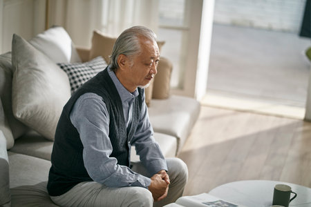 sad asian senior man sitting on couch in living room at homeの写真素材