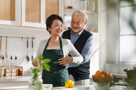 loving senior asian man husband helping wife tying up apron in kitchen at homeの写真素材