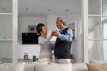 loving romantic senior asian couple dancing in living room at homeの写真素材