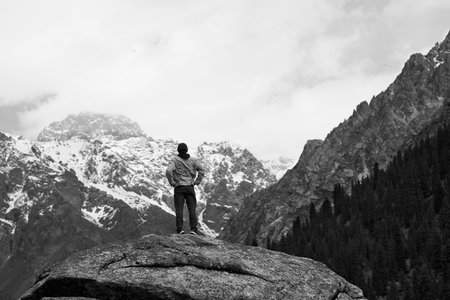 rear view of asian man male traveler standing on top of a rock looking at a snow mountain in...