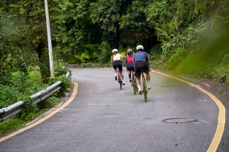 rear view of group of three young asian adult cyclists riding bike outdoors on rural roadの写真素材