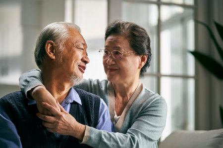 portrait of happy loving senior asian couple sitting on couch at homeの写真素材