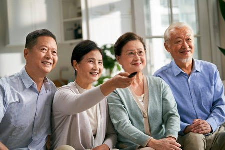 group of happy senior asian people two couples sitting on couch at home watching tv together