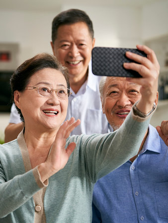 group of happy senior asian people sitting on family couch at home taking a selfie together using...