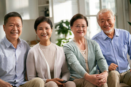 group of happy senior asian people two couples sitting on couch at home watching tv togetherの写真素材