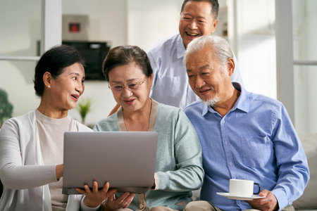 group of happy senior asian people sitting on couch at home using laptop computer togetherの写真素材