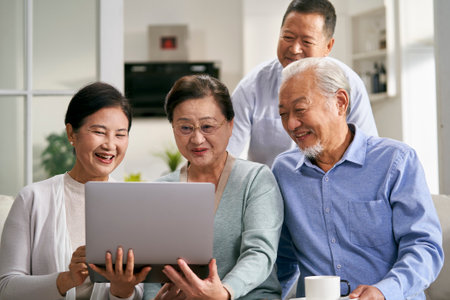 group of happy senior asian people sitting on couch at home using laptop computer togetherの写真素材