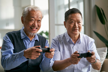 two happy senior asian men sitting on couch at home playing video game togetherの写真素材