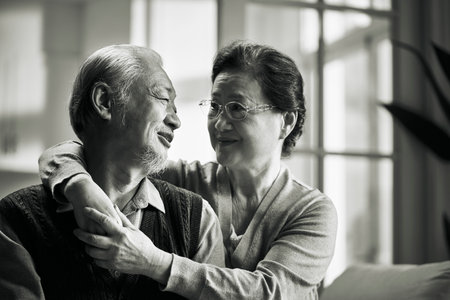 black and white portrait of happy loving senior asian couple sitting on couch at homeの写真素材