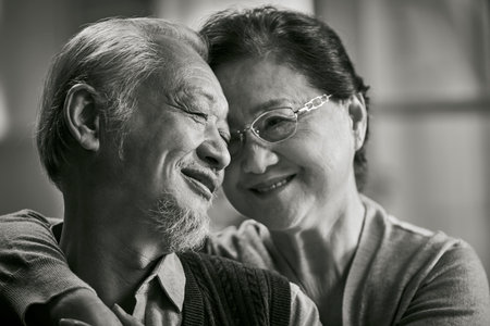 black and white portrait of happy loving senior asian couple sitting on couch at homeの写真素材