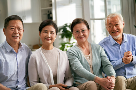group of happy senior asian people two couples sitting on couch at home watching tv togetherの写真素材