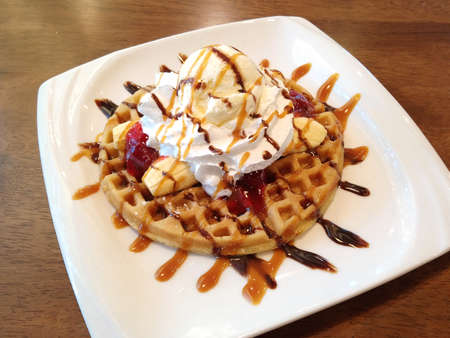 Banana split with whip cream, ice cream, strawberry jam and syrup on top of waffle dessert menuの写真素材