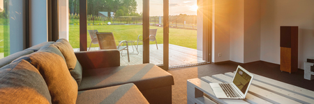 New living room with big windows, garden view and sun rays, panoramaの写真素材