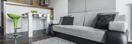 Panoramic view of big comfortable grey sofa and dining table with chairs in modern apartment