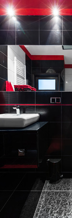 Vertical panorama of bathroom interior with black tiles, red details and white basinの写真素材