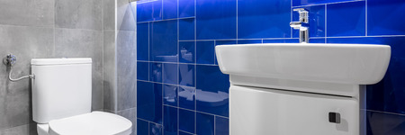 Panorama of bathroom with grey matt tiles and blue glossy tiles, white toilet and sinkの写真素材