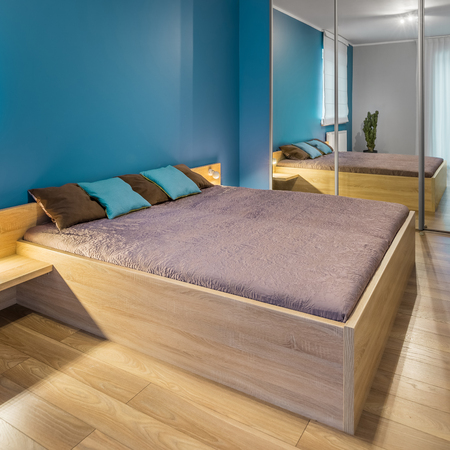 Spacious blue bedroom with big wooden bed and mirrored wardrobeの写真素材