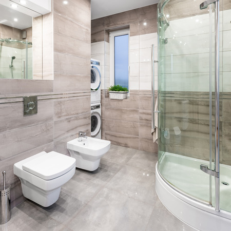 Spacious high-gloss bathroom with mirror, toilet, bidet, shower, washer and clothes dryerの写真素材