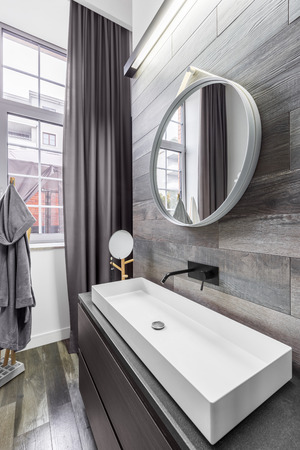 Dark bathroom with countertop basin and round mirrorの写真素材