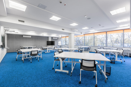 Bright university communal study room with white desks, chairs and big tvの写真素材