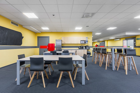 Modern lunchroom interior with wooden tables and black chairs, kitchenette in backgroundの写真素材