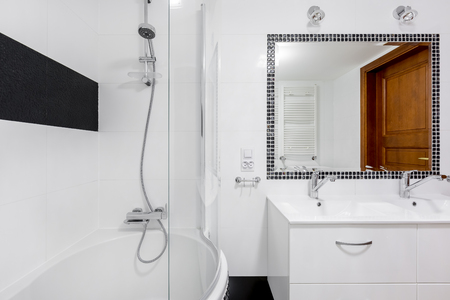 White luxury bathroom interior with big mirror, two faucets and bathtub with showerの写真素材