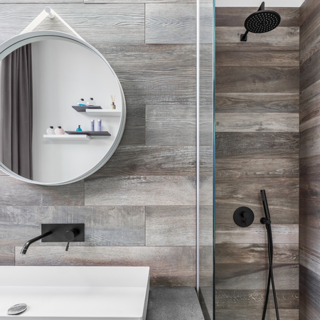 Modern bathroom with shower, round mirror and wood effect tilingの写真素材