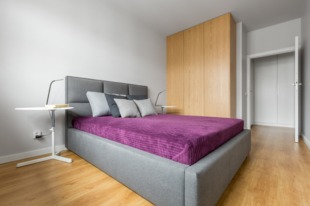 Bedroom designed in minimalist style with big grey bed and high wooden wardrobeの写真素材