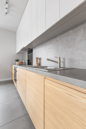 Contemporary wooden brown and white kitchen furniture with long grey worktop and silver tapの写真素材