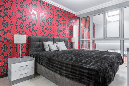 Fancy bedroom with double bed, nightstand, window, black and red ornament wallpaperの写真素材