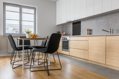 Modern kitchen with long countertop, table, chairs and wooden floor panelsの写真素材