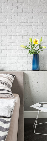 Vertical panorama of flowers in blue vase in simple bedroom with white brick wallの写真素材