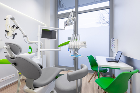 White interior with modern dental unit with green chair, led lamp and computerの写真素材