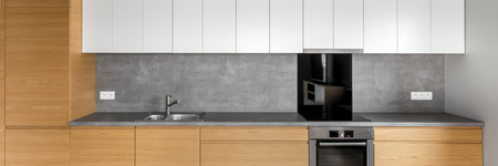 Modern kitchen with wooden cabinets, granite worktop, white cupboards and concrete wall, panoramaの写真素材