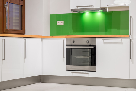 Small kitchen area with green wall, wooden worktop, white furniture and built-in stoveの写真素材