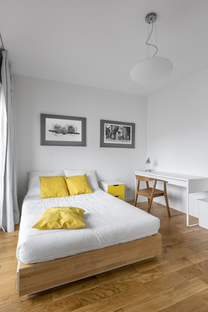 Modern white bedroom with big wooden bed, desk and yellow decorationsの写真素材