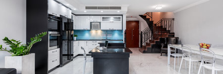 Modern and functional home interior with open kitchen, dining table and stairs, panorama