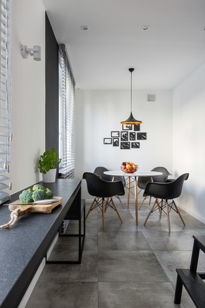 Modern, white kitchen with long, granite countertop, round table and chairsの写真素材