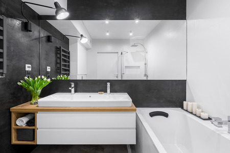 Black and white bathroom with big mirror, bathtub, lighting and countertop double basinの写真素材