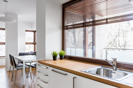 White kitchen with wooden countertop, silver sink and big window with blindsの写真素材