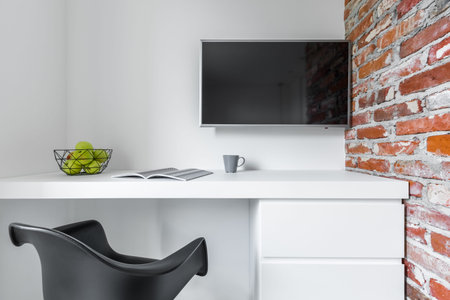 White room with modern countertop desk, black chair, tv and brick wallの写真素材