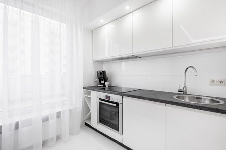 Modern, white kitchen with black countertop, sink, cupboards and windowの写真素材