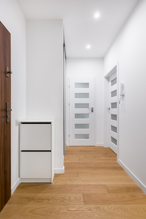 White entryway with light, wooden floor and dark, wooden doorの写真素材