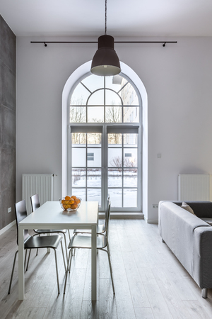 White loft interior with half circle window, dining table and chairsの写真素材