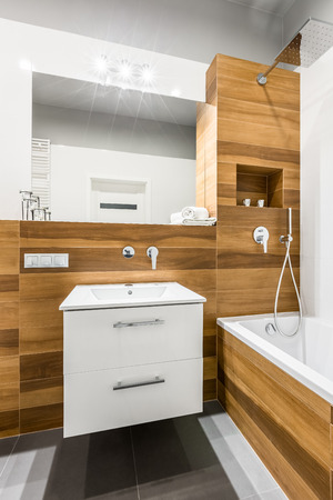 Wooden bathroom with bathtub, mirror, washbasin and cabinetの写真素材