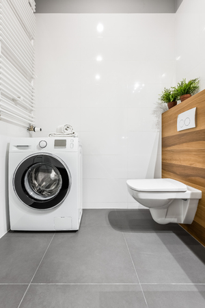 Modern white bathroom with toilet, washer and wooden wallの写真素材
