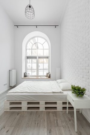 White bedroom with pallet bed and brick wallの写真素材