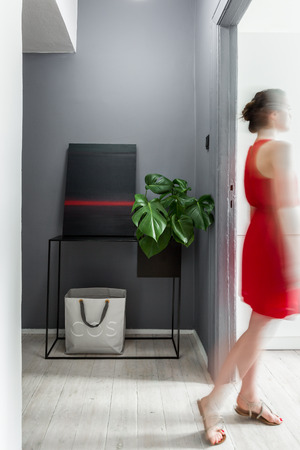 Woman wearing red dress standing in modern apartment with decorative paintingの写真素材